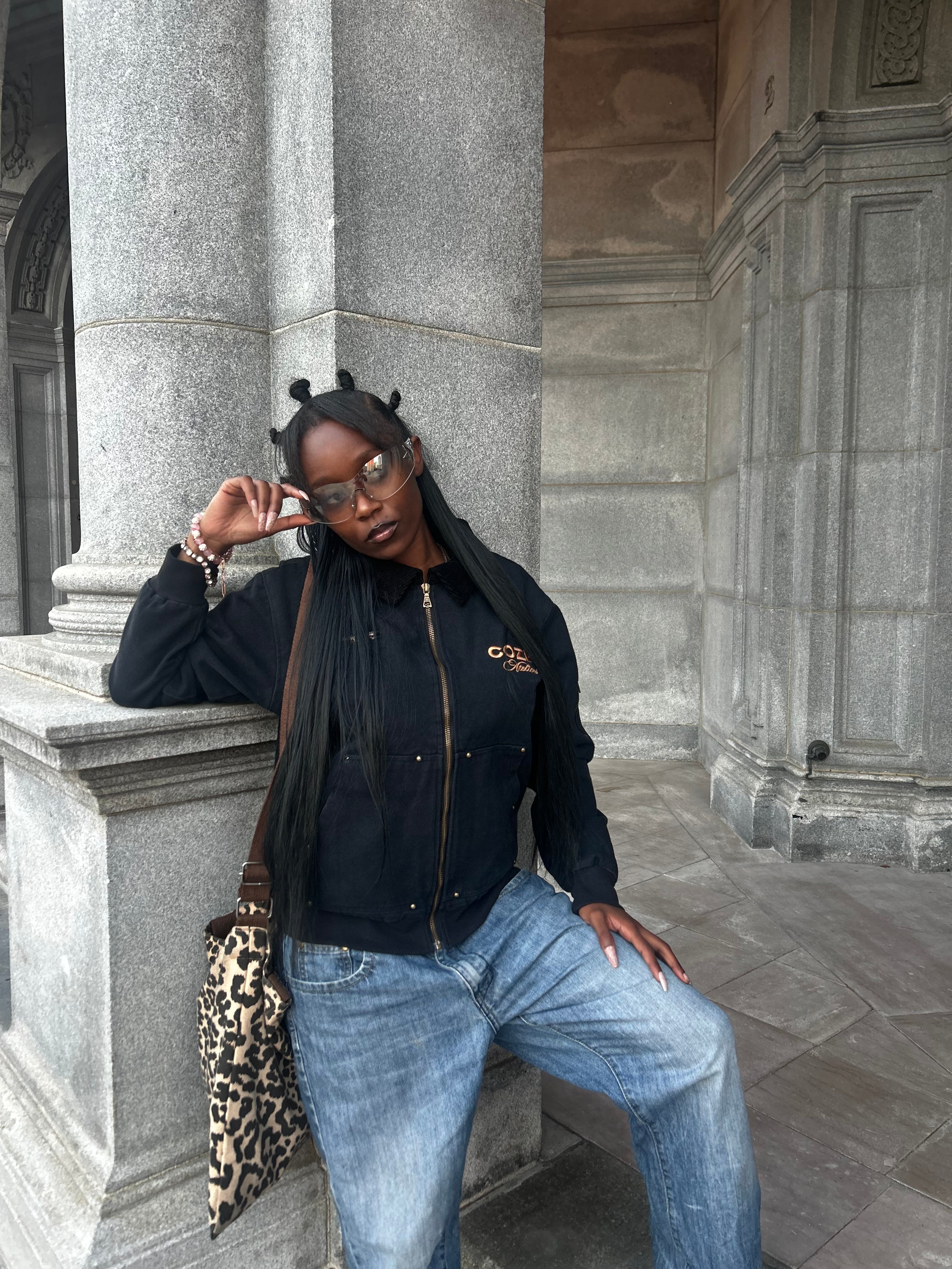 Person wearing a black jacket and blue jeans standing on stone steps.