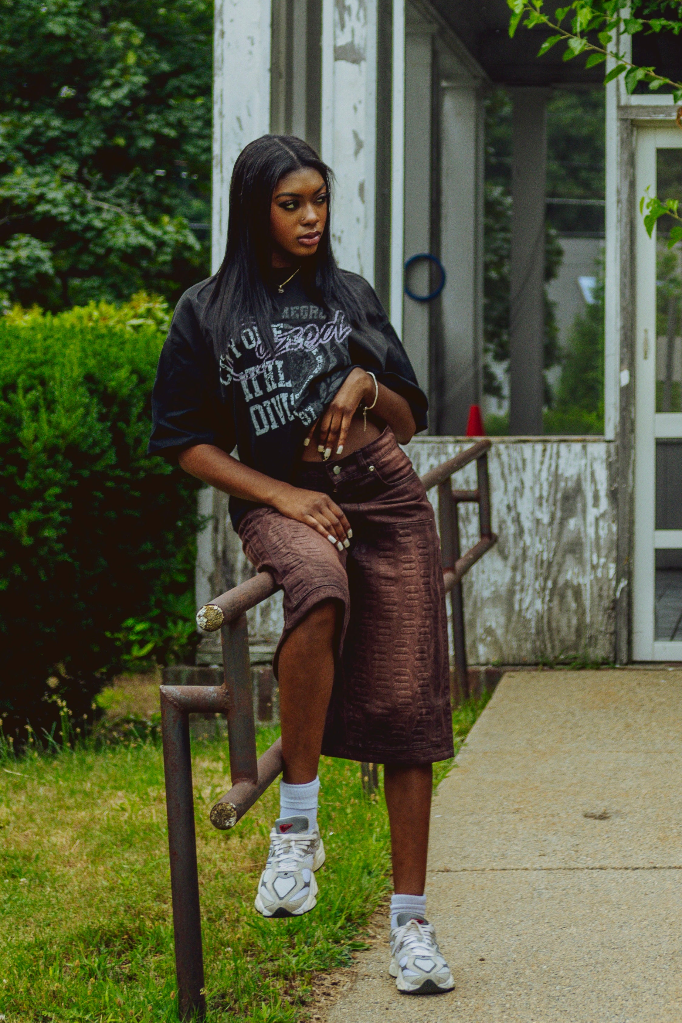 Person sitting on a chair outdoors wearing a black shirt and brown jean shorts.