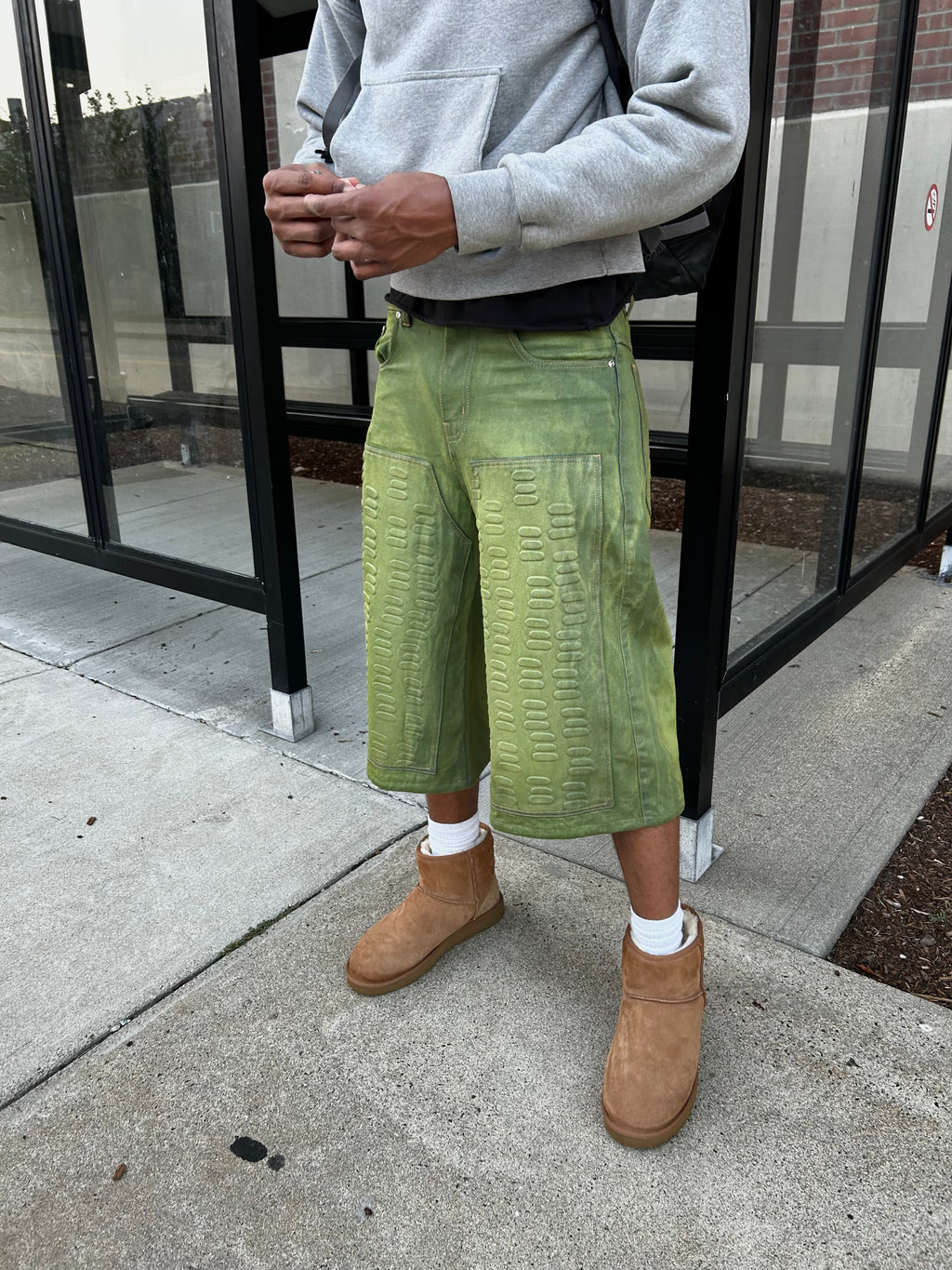 Person wearing green textured pants and brown boots on a sidewalk.